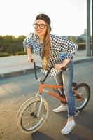 adorável jovem mulher dentro uma chapéu equitação uma bicicleta em cidade fundo dentro a luz solar ao ar livre foto