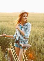 adorável jovem mulher carrinhos dentro uma campo com dela bicicleta foto