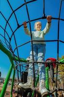 uma feliz ativo dez ano velho menina escalou uma corda rede em uma Parque infantil contra uma brilhante azul céu em uma ensolarado dia foto