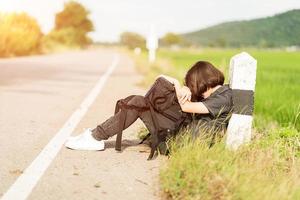 mulher sente-se com mochila pedindo carona ao longo de uma estrada foto