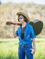 mulher usa chapéu e carrega seu violão no campo de grama foto