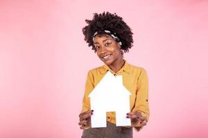 seguro, empréstimo, real Estado e família conceito. alegre africano americano fêmea comprando ou vendendo lar, segurando papel casa e sorridente otimista, procurando para Novo apartamento, branco fundo foto