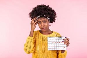 jovem africano americano mulher segurando menstruação calendário sobre isolado fundo com surpresa face. mulher segurando menstruação calendário com confuso face, receoso e animado com medo expressão foto