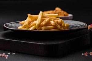 delicioso crocantes francês fritas com sal e especiarias em uma Sombrio concreto fundo foto