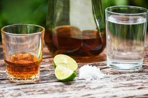 alcoólico bebidas e limão sal em rústico madeira fundo conhaque dentro uma vidro com álcool garrafas e água vodka rum conhaque tequila e uísque conceito foto