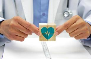 mão segurando uma de madeira quadra cubo com cuidados de saúde médico símbolo, coração taxa ícone. médico e saúde conceito.