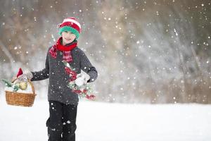 uma feliz criança antes Natal com Natal brinquedos anda em através a floresta debaixo uma queda de neve. foto