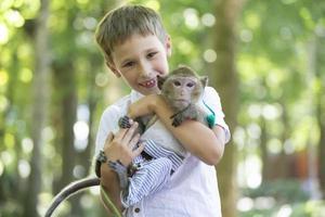 uma feliz Garoto detém uma pequeno macaco dentro dele mãos. foto