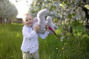 uma criança feliz em um jardim florido segura um urso de brinquedo. foto