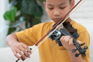 uma criança asiática tocando e praticando violino instrumento musical de cordas contra em casa, conceito de educação musical, inspiração, estudante de escola de arte adolescente. foto