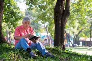 feliz ásia velho Senior homem com cinzento cabelo lendo livro lado de fora dentro parque. conceito do feliz idosos homem depois de aposentadoria e Boa saúde foto