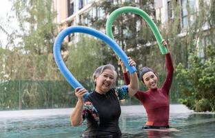 jovem treinador ajudando Senior mulher dentro aqua aeróbica e trabalhando Fora dentro a piscina. velho mulher e maduro homem fazendo aqua aeróbica exercício dentro natação piscina, idosos Esportes, e ativo estilo de vida conceito. foto