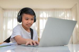 menino asiático tocando violão e assistindo curso online no laptop enquanto pratica para aprender música ou instrumento musical online em casa. os alunos estudam on-line com os professores de videochamada tocam violão. foto