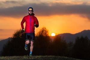 homem atlético com barba correndo nas montanhas durante um pôr do sol colorido de fogo foto