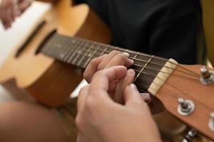 ásia Garoto jogando guitarra com mãe dentro a vivo quarto para ensino ele filho jogar guitarra, sentir estimado e encorajado. conceito do uma feliz família, Aprendendo e Diversão estilo de vida, amor família laços foto