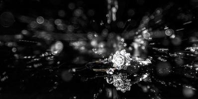 uma diamante noivado e uma Casamento anel em uma reflexivo superfície com água espirrando baixa a partir de acima. foto