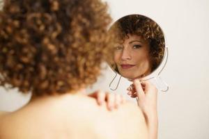 adulto fêmea com encaracolado vermelho cabelo olhando às a Câmera a partir de a reflexão dentro dela Maquiagem espelho foto