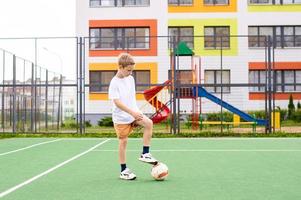 uma Adolescência Garoto carrinhos em uma verde campo dentro a escola Jardim com uma futebol bola dentro Treinamento foto