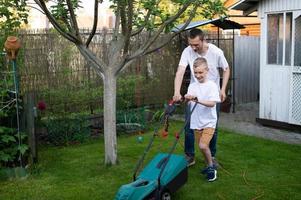 Papai e dele curioso filho Cortar a verde gramado perto a casa. foto