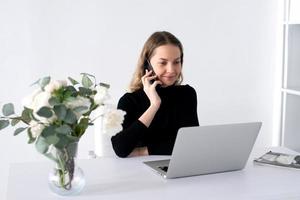 a menina trabalho dentro uma branco escritório com uma computador portátil e flores em a mesa foto