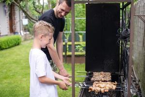 alegre Papai e filho assado carne em a grade foto