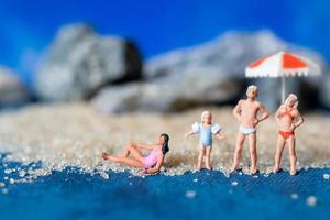 pessoas em miniatura usando maiôs relaxantes na praia com um fundo azul, conceito de verão foto