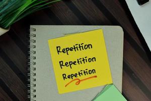 repetição, repetição, repetição escrita em nota adesiva isolada na mesa de madeira foto