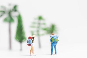 viajantes em miniatura com mochilas caminhando sobre um fundo branco, conceito de viagem e aventura foto