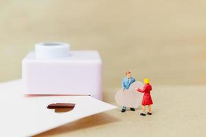 casal em miniatura com um coração de papel sobre fundo de madeira, conceito de dia dos namorados foto