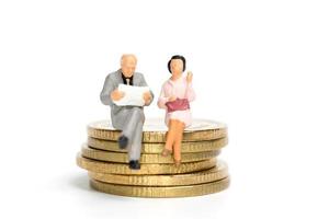 empresários em miniatura sentados sobre uma pilha de moedas, dinheiro e conceitos financeiros foto