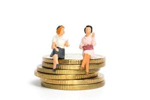 empresários em miniatura sentados sobre uma pilha de moedas, dinheiro e conceitos financeiros