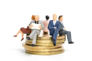 empresários em miniatura sentados sobre uma pilha de moedas, dinheiro e conceitos financeiros