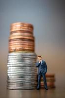 empresário em miniatura parado com uma pilha de moedas, conceito de crescimento do negócio foto