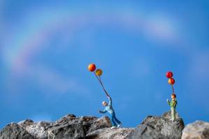 família em miniatura segurando balões em uma rocha com um fundo de céu azul foto