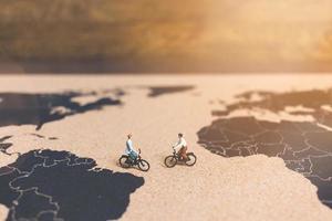 viajantes em miniatura andando de bicicleta em um mapa-múndi, viajando e explorando o conceito do mundo foto
