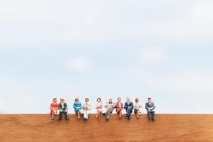 grupo em miniatura de empresários sentados em um chão de madeira com um fundo de céu azul foto