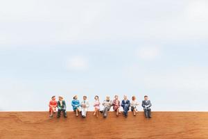 grupo em miniatura de empresários sentados em um chão de madeira com um fundo de céu azul