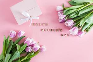 uma festivo composição com roxa tulipas e texto dentro de madeira cartas do feliz mãe dia. topo visualizar. plano estilo. Rosa fundo. foto