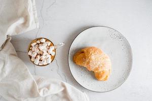 fresco croissant em uma prato e uma grande copo do café em a mesa. caseiro café da manhã estilo de vida. topo Visão