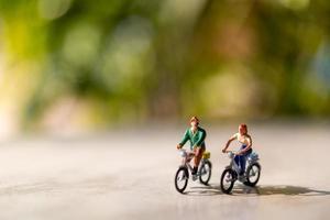 pessoas em miniatura andando de bicicleta ao ar livre com um fundo verde bokeh, conceito de esporte e viagem