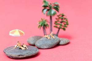 pessoas em miniatura usando maiôs relaxando em uma rocha com um fundo rosa foto