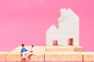 casal em miniatura com casas em um fundo rosa, conceito de dia dos namorados foto