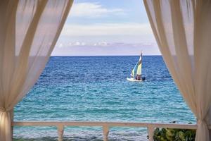 uma romântico Visão do barco a vela Navegando ao longo a atlântico costa, Cuba. arqueado sacada com branco cortinas. foto