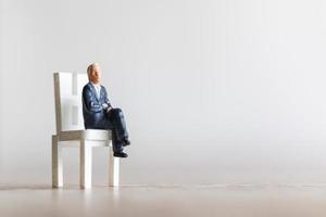 empresário em miniatura sentado em uma cadeira com um fundo desfocado foto