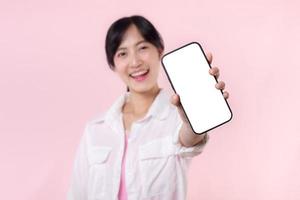 feliz sorridente jovem ásia mulher recomendando mostrando Novo inscrição ou Móvel anúncio, brincar Smartphone modelo bandeira isolado em Rosa fundo. colagem em branco tela digital Móvel dispositivo. foto