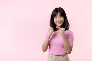 retrato lindo jovem ásia mulher feliz sorrir com punho acima vitória gesto expressão alegre dela sucesso realização contra Rosa pastel estúdio fundo. mulher dia vencedora celebração conceito. foto