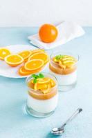 laranja Panna cotta com hortelã folha dentro óculos e laranja fatias em uma prato em uma luz mesa. doce italiano sobremesa. vertical Visão foto