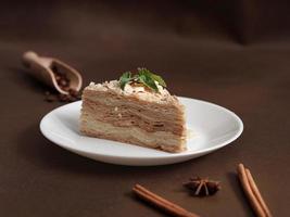 delicioso napoleão bolo com creme em uma branco prato decorado com uma raminho do hortelã em uma Castanho fundo. uma canela grudar, badyan, café feijões em uma Castanho fundo. cópia de espaço foto