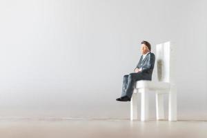 empresário em miniatura sentado em uma cadeira em um fundo branco foto