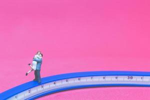 casal em miniatura se abraçando em uma ponte com um fundo rosa foto